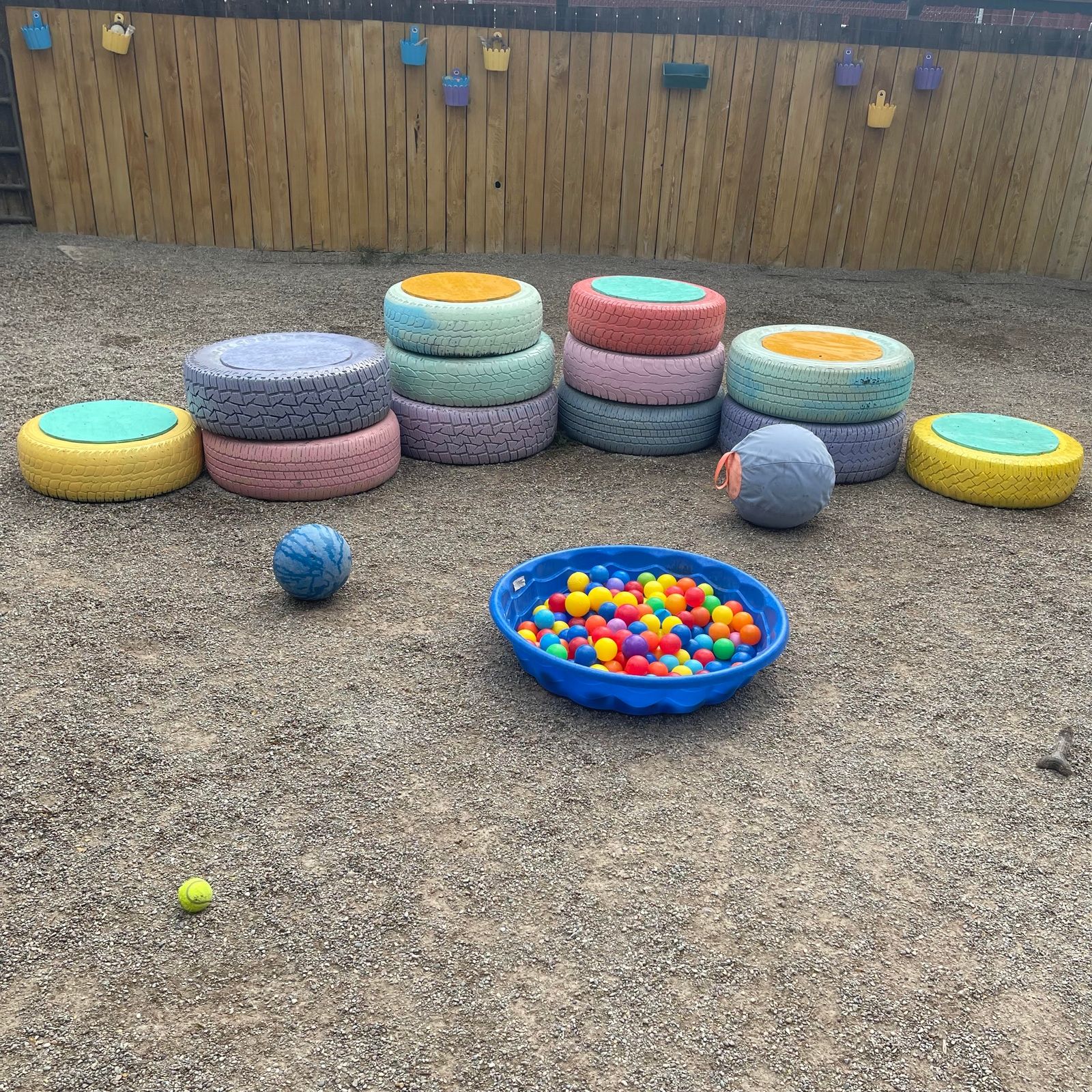 Fenced gravel play yard with painted tire stacks and a ball pit for the boarding dogs